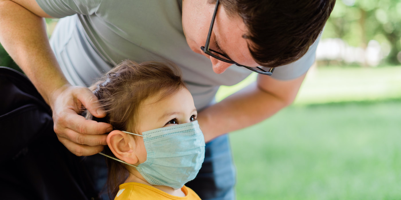Image of adult man helping toddler put on a protective facial covering.