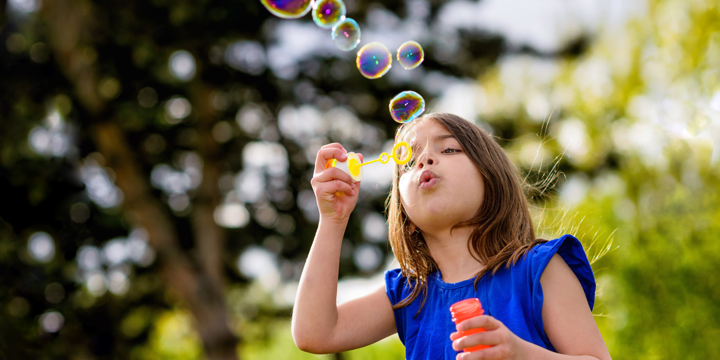 Image of young girl blowing soap bubbles on a sunny day.