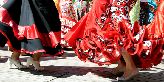 Image of skirts and feet of women in traditional flamenco dresses.