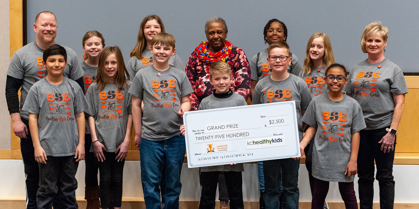 A group of children and adults in matching t-shirts pose for a photo with a check for $2,500