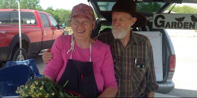 A man and woman pose for a photo at their farmers market booth.