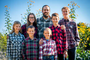 Image of parents and 5 children all wearing plaid shirts while standing in a field.